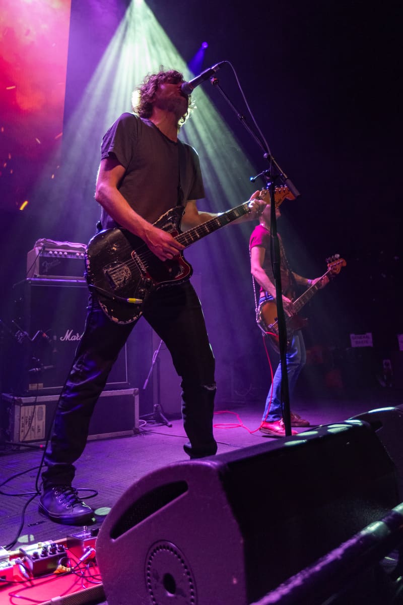 Guitarist performing on stage under purple and pink spotlights during Jebediah's Gum Up The Bearings 2023 Tour.