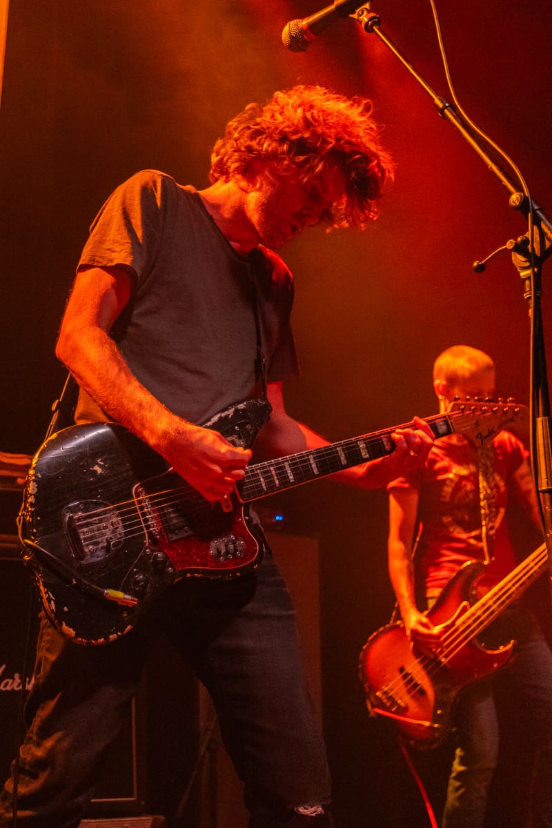 Guitarist and bassist perform on stage bathed in warm orange and red stage lighting during the Jebediah tour.