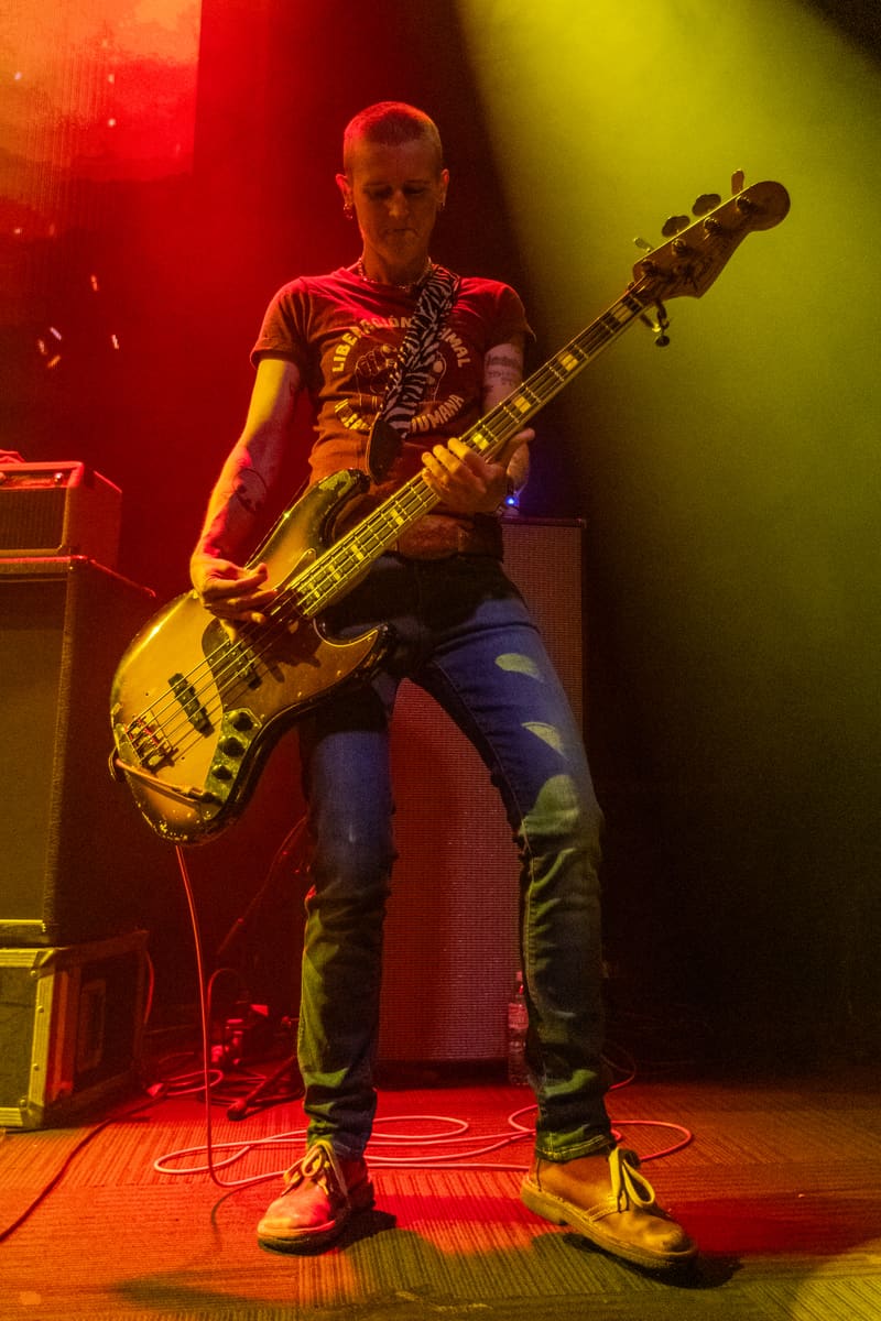 Bass guitarist performing on stage bathed in red and yellow stage lighting during Jebediah's Gum Up The Bearings 2023 tour.