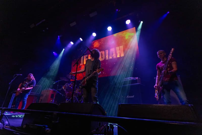 Jebediah band members perform on stage illuminated by blue and warm-toned spotlights during the Gum Up The Bearings 2023 tour.