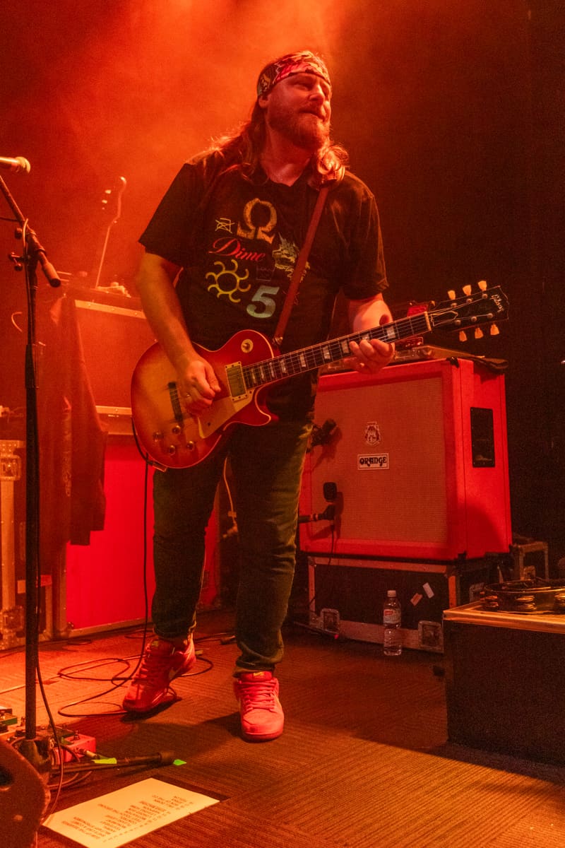 Guitarist performs on stage bathed in warm red and orange lighting during Jebediah's Gum Up The Bearings 2023 tour.