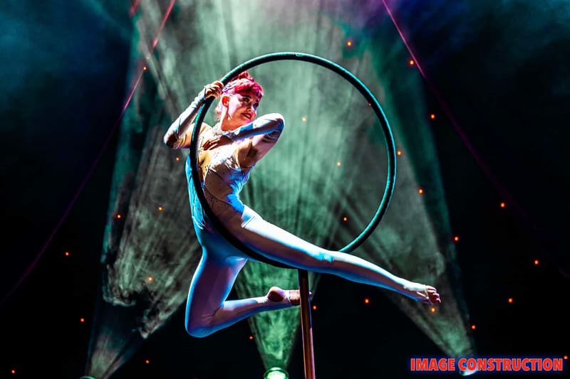 Aerialist suspended within a large hoop against green atmospheric lighting during The Christmas Spectacular.