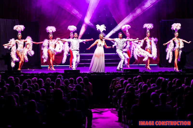 Performers in sequined costumes dance in unison across a stage bathed in purple light during The Christmas Spectacular.