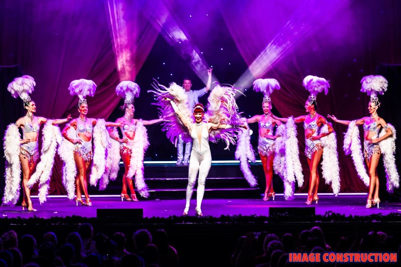 Dancers in sequined costumes perform under purple stage lighting during The Christmas Spectacular production.