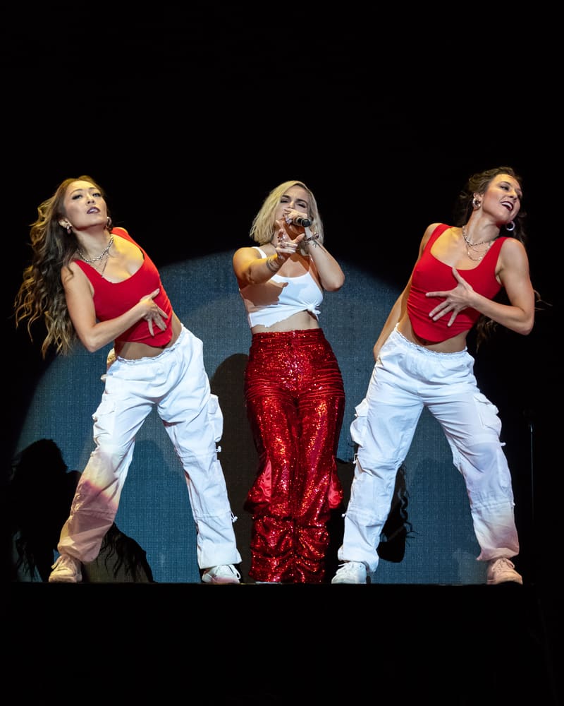 Three performers on stage during Jojo – Fridayz Live, two in red and white outfits flanking a central dancer in a red sequinned skirt.