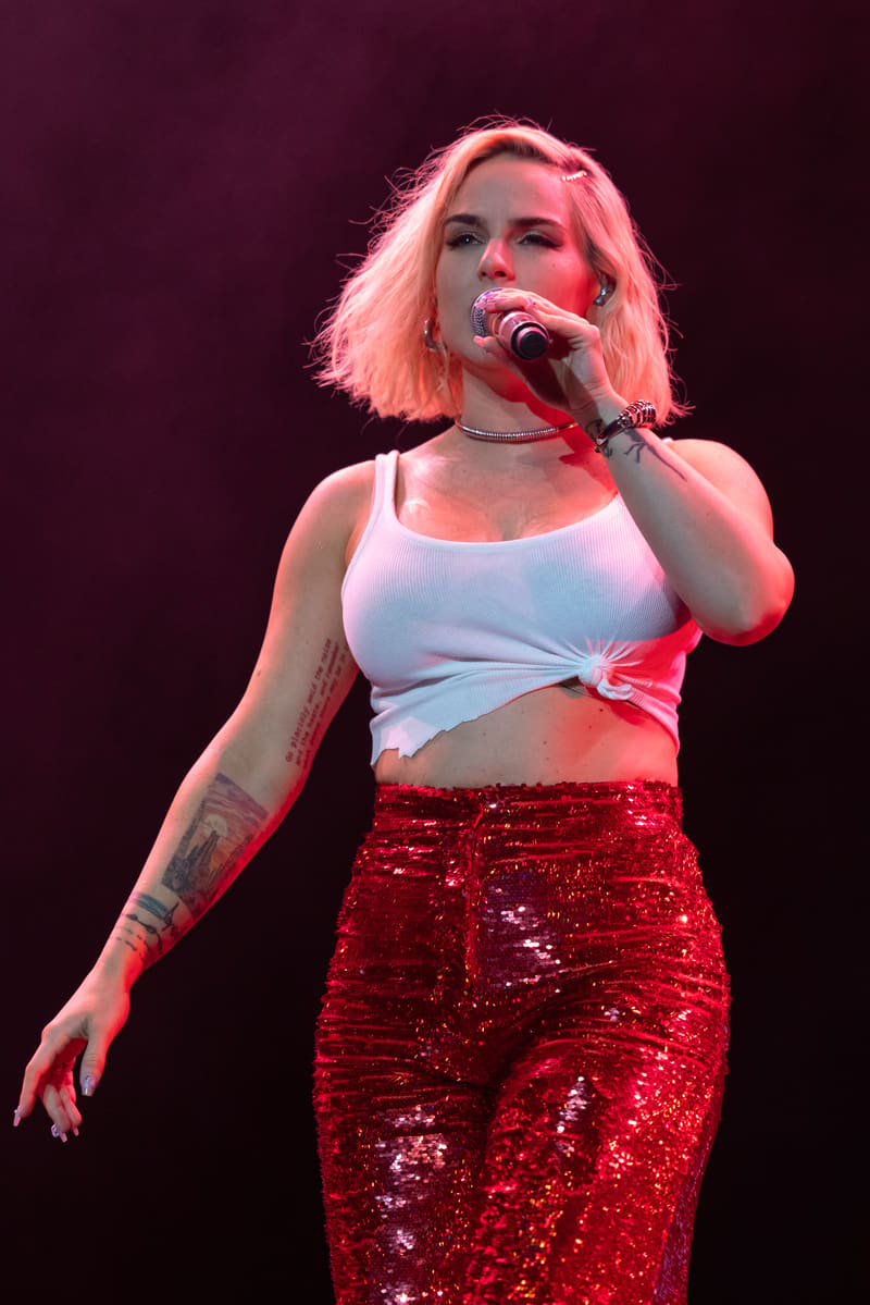 Singer performing at microphone in white crop top and red sequinned skirt, lit by pink stage lighting.