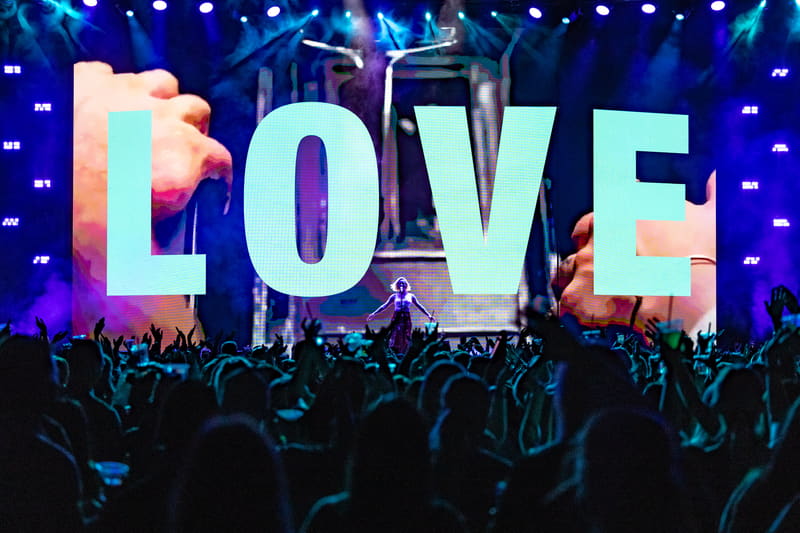 Crowd of concertgoers silhouetted against large illuminated "LOVE" letters on stage during Fridayz Live event.