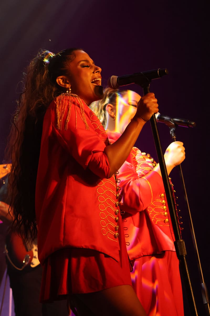 Performer singing into microphone on stage in red dress with warm stage lighting during a live performance.