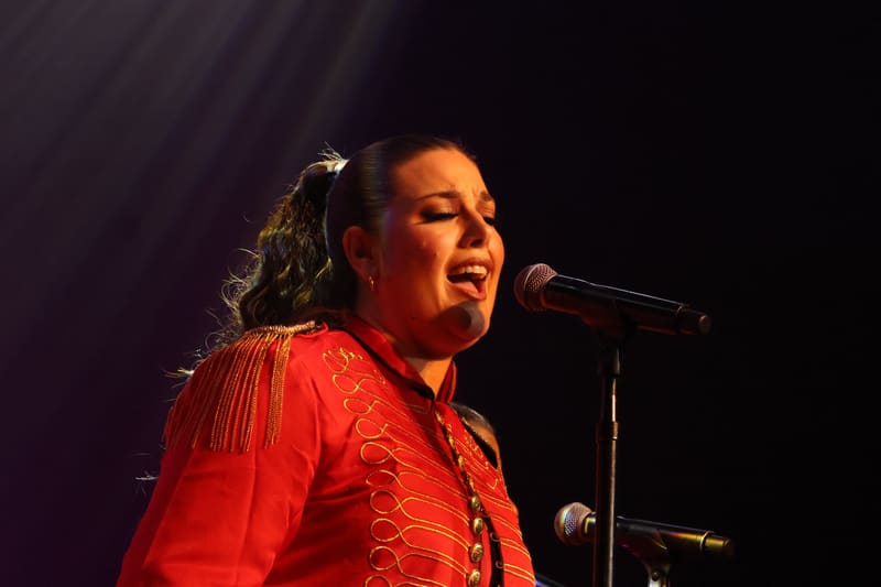 Performer in a bright red sequinned jacket singing into a microphone under warm stage lighting.