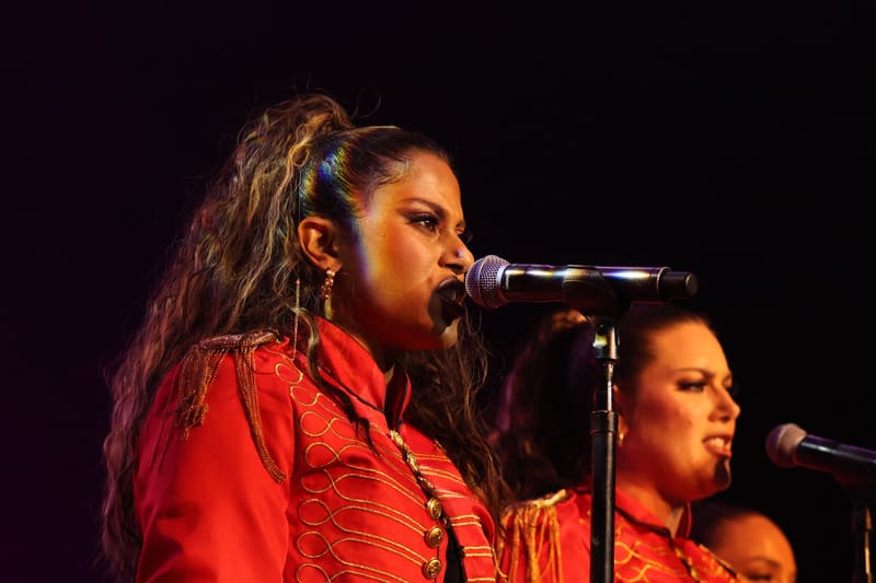 Two performers in red jackets sing at microphones on a darkened stage.