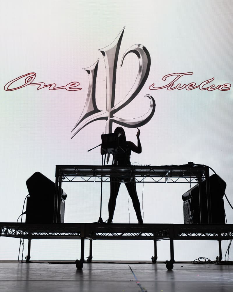 Silhouetted performer stands on elevated stage platform beneath large stylised "112" logo during live performance.