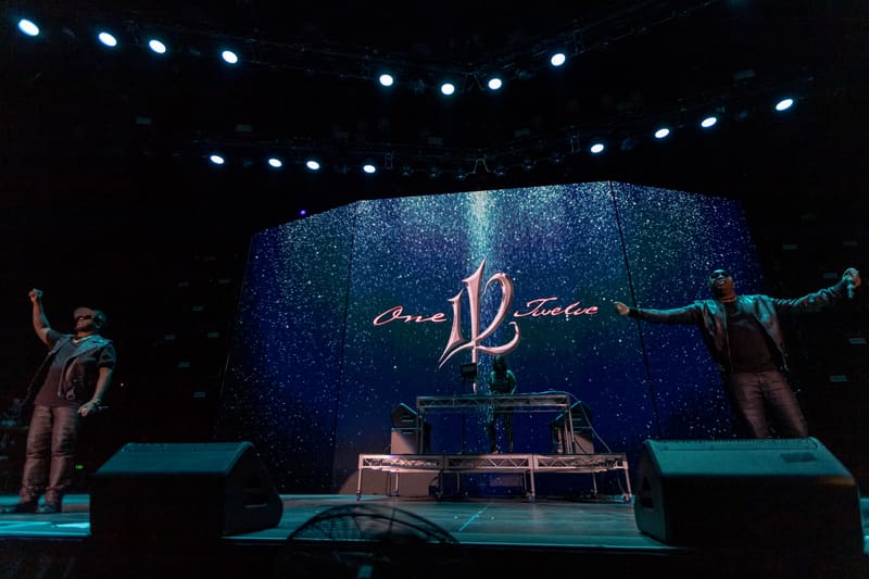 Performer on elevated stage platform under blue lighting with "112" logo displayed behind during live music event.