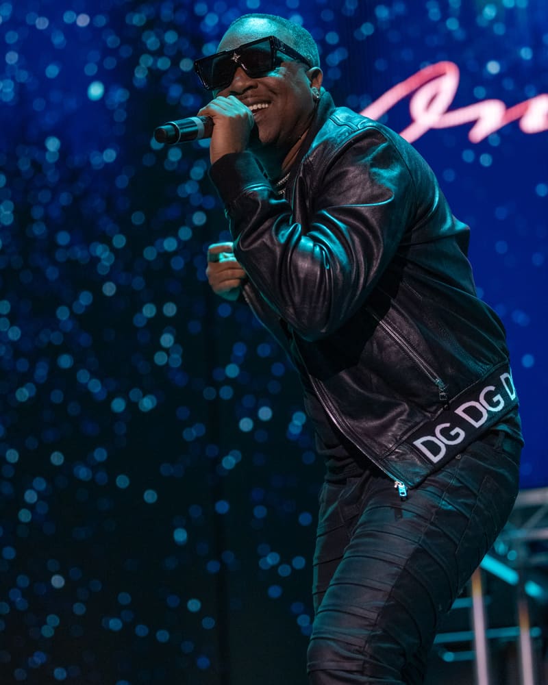 Performer singing into microphone on stage with blue bokeh lighting and sparkles behind.