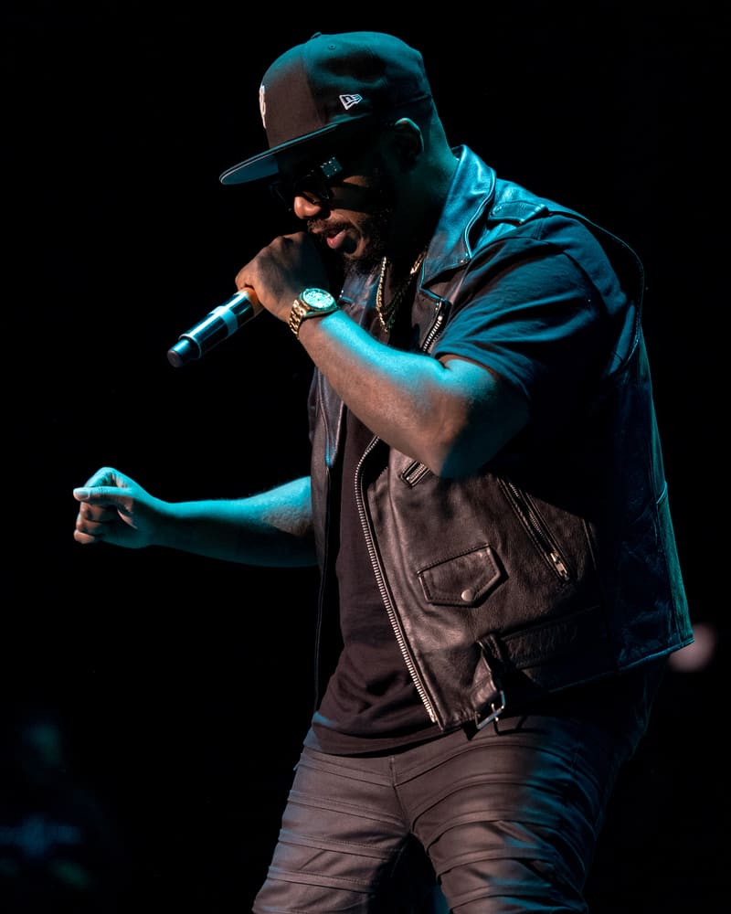 Performer raps into microphone under blue stage lighting at 112 – Fridayz Live.