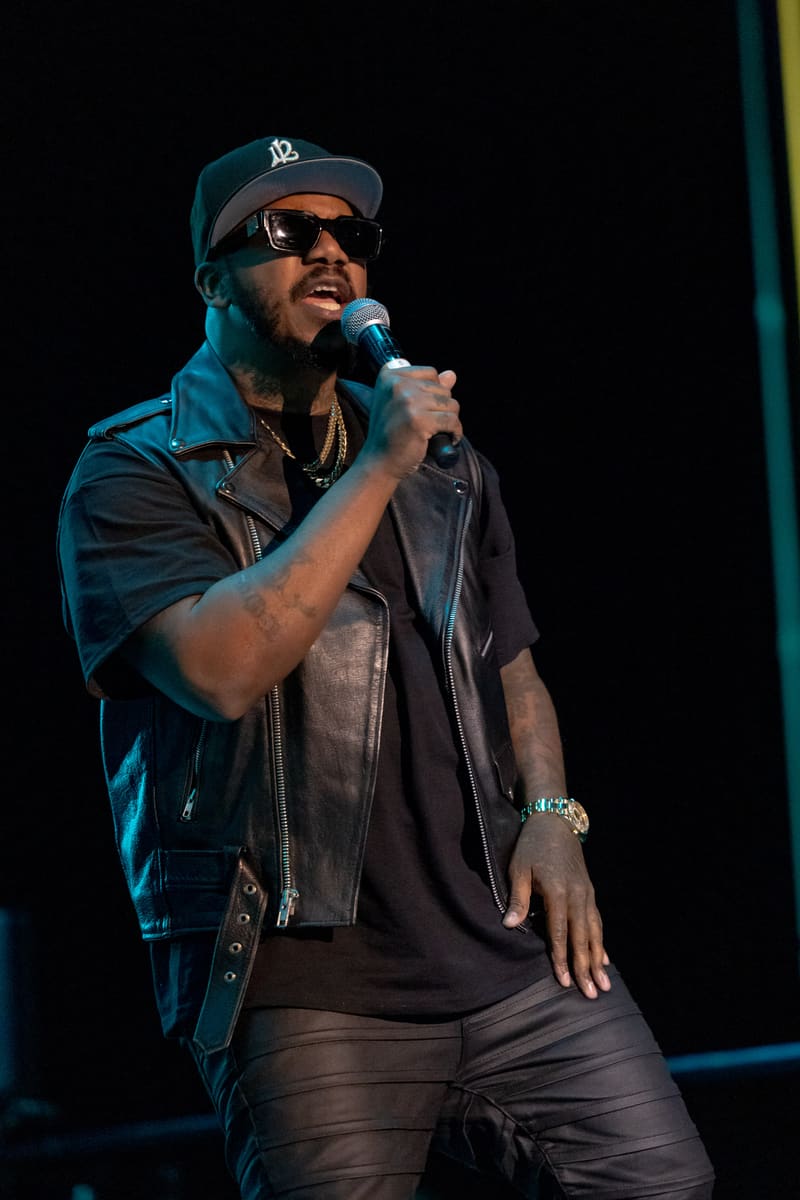 Performer wearing sunglasses and cap singing into microphone under blue stage lighting at 112 – Fridayz Live.