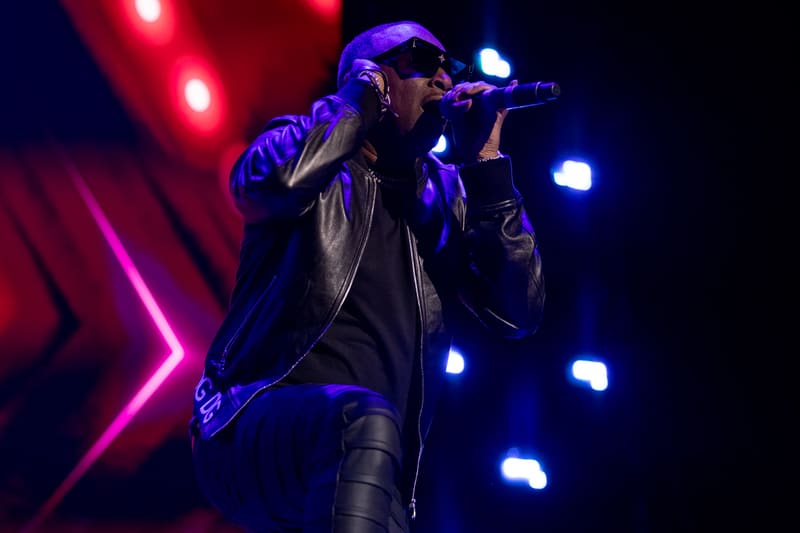 Performer singing into microphone on stage beneath vibrant pink and blue stage lighting.