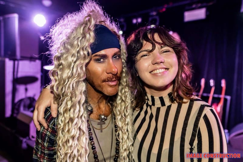 Two performers with long curly blonde and dark wavy hair smile together on stage lit by purple spotlights during the Pierce Brothers Moonrise 2026 Album Tour.