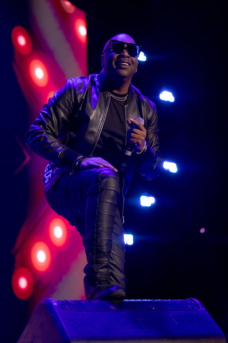 Performer in black leather jacket and sunglasses singing on stage, bathed in vibrant red and blue stage lighting.