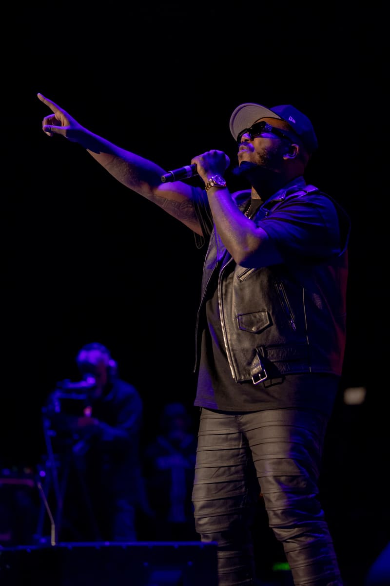 Performer in blue cap and vest gestures to audience under purple stage lighting at 112 – Fridayz Live.