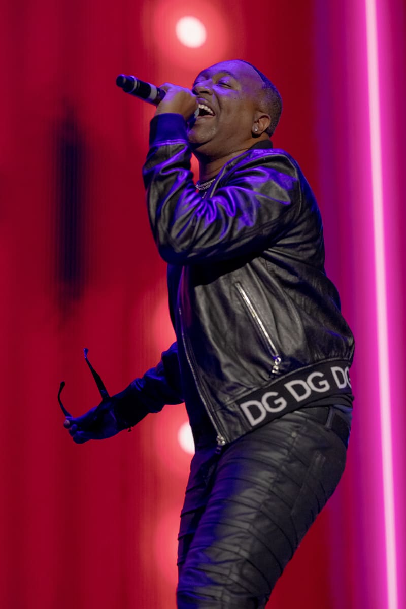 Performer singing into microphone on stage at Fridayz Live, bathed in red and purple neon lighting.