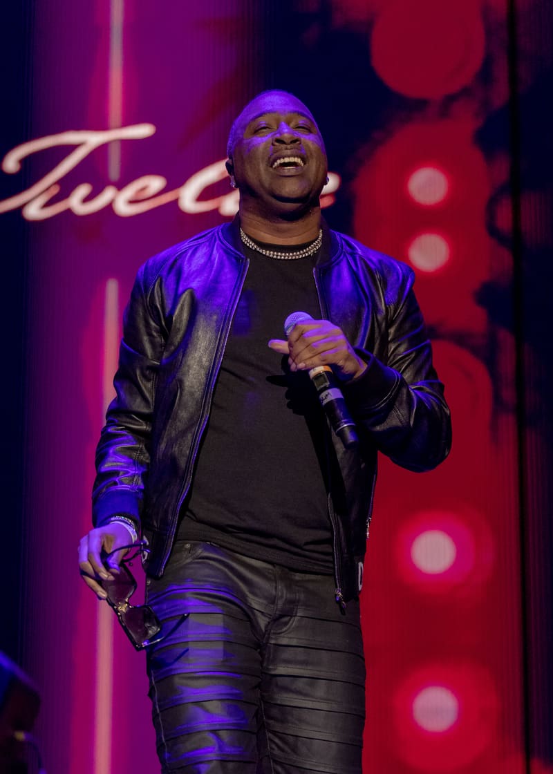 Performer on stage at 112 – Fridayz Live, illuminated by purple and red stage lighting, holding a microphone whilst smiling.