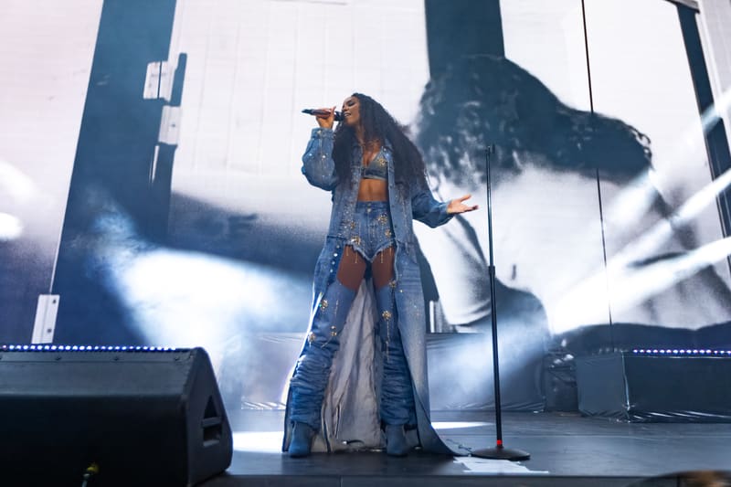 Performer in a sequined denim jacket singing on stage under blue spotlights with dramatic shadow projection.