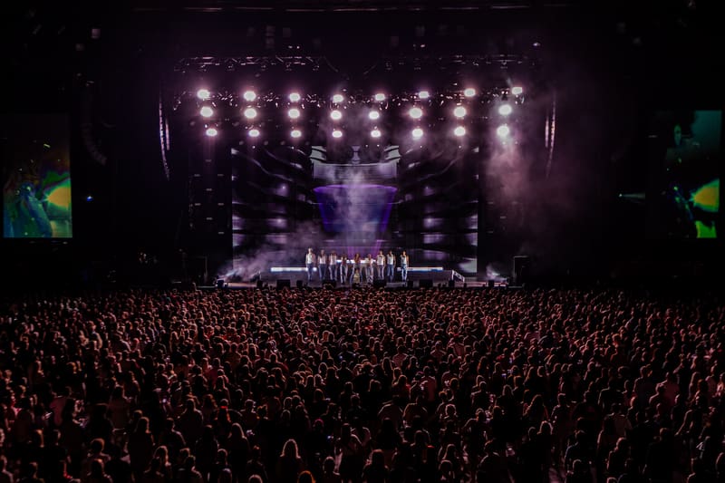 Massive crowd faces a stage lit by rows of bright spotlights during an evening concert performance.