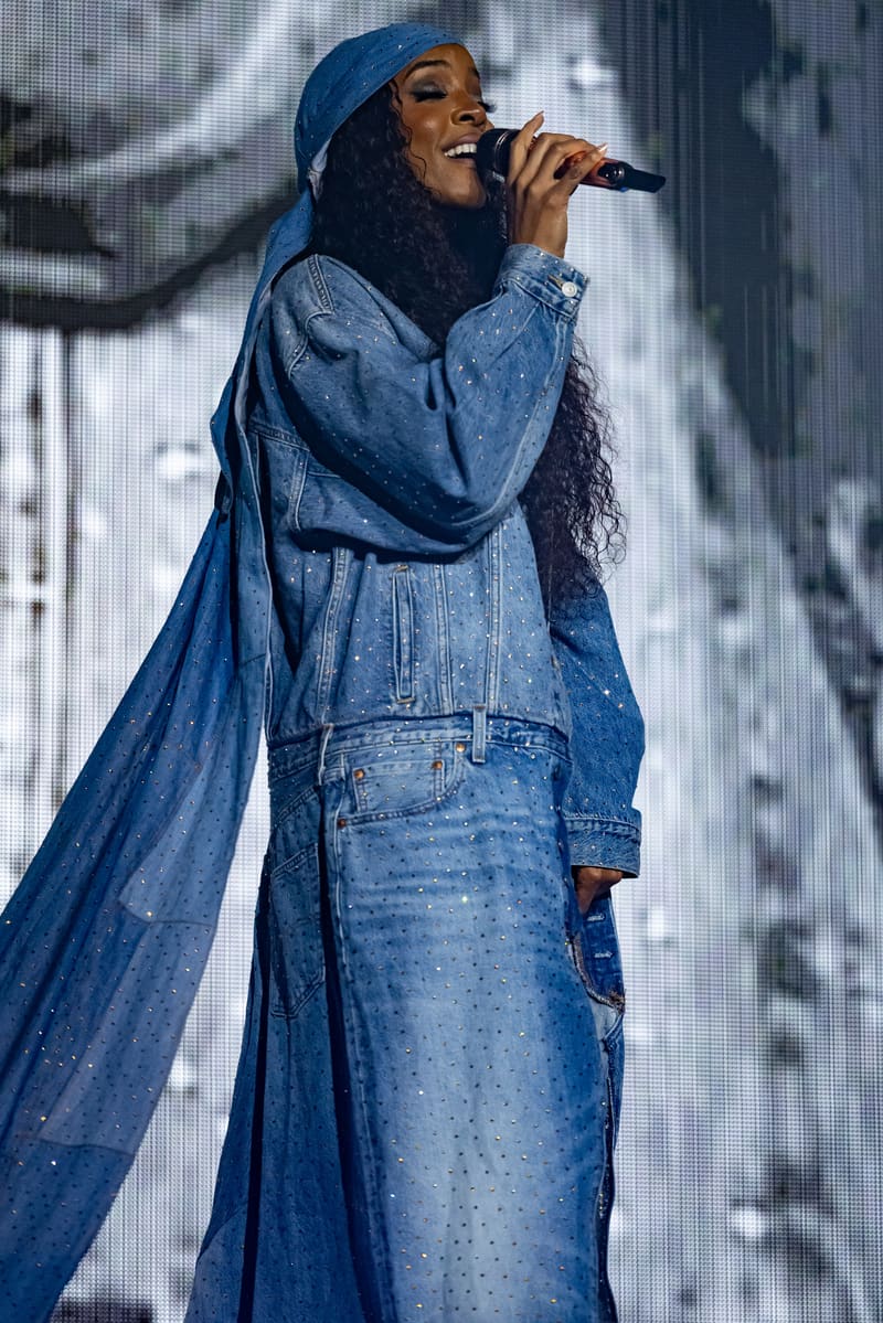 Singer in denim jacket and coordinating blue headwrap performing with microphone on stage.
