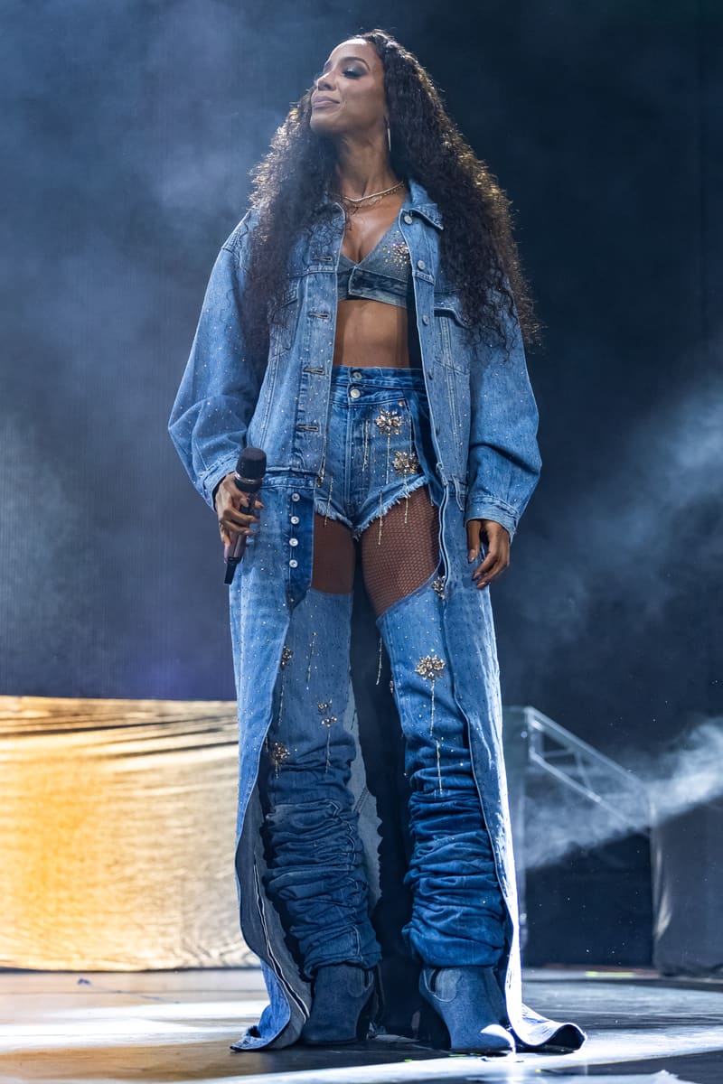 Performer in denim outfit stands on stage under blue lighting during a live concert performance.