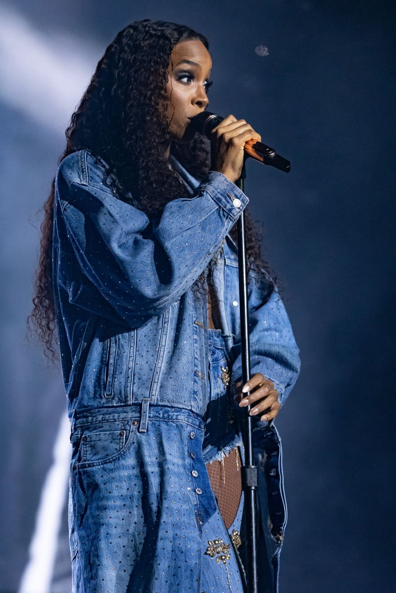 Singer performing at microphone in denim jacket under blue stage lighting.