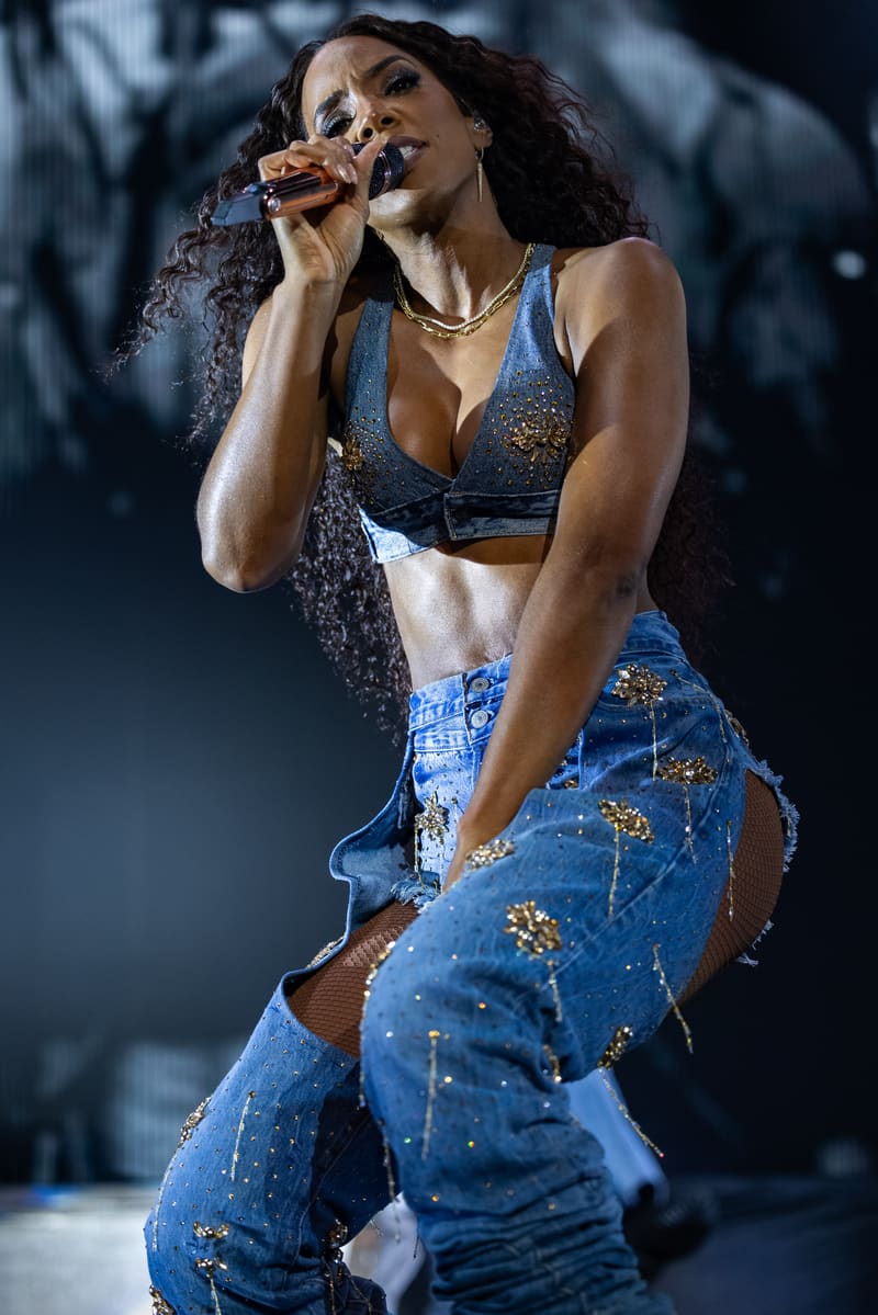 Singer performing at microphone in blue sequined outfit under stage lighting.