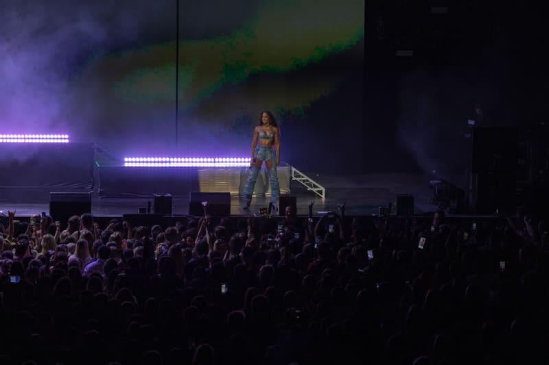 Solo performer on stage beneath neon lighting, surrounded by an engaged crowd holding mobile phones.