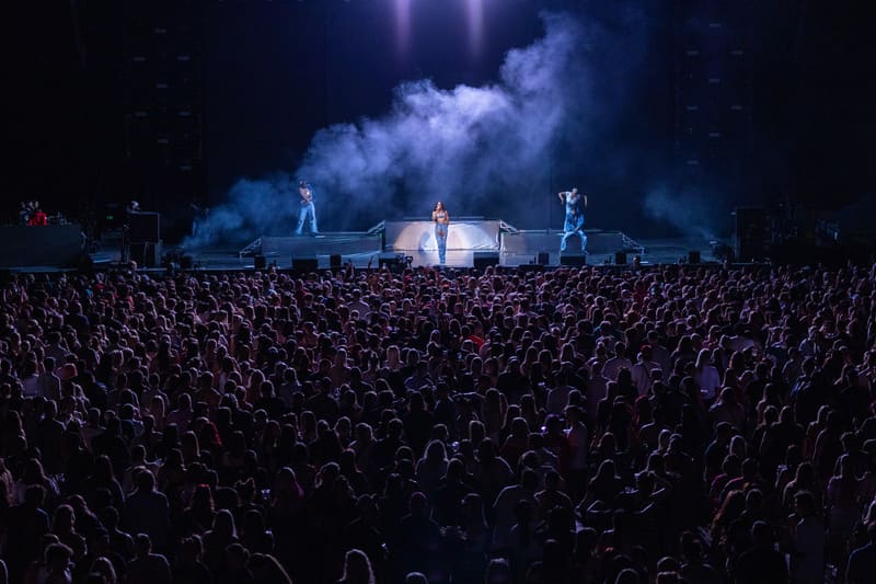 Large crowd watches performers on an illuminated stage engulfed in blue smoke and dramatic lighting.