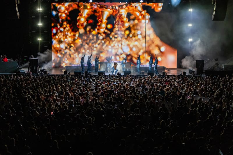 Large crowd silhouetted against illuminated stage with golden confetti cannon burst at Fridayz Live concert.