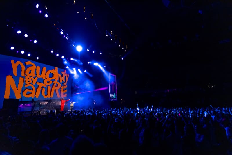 Large stage with "Naughty by Nature" signage illuminated in orange, crowd silhouetted against blue stage lighting.