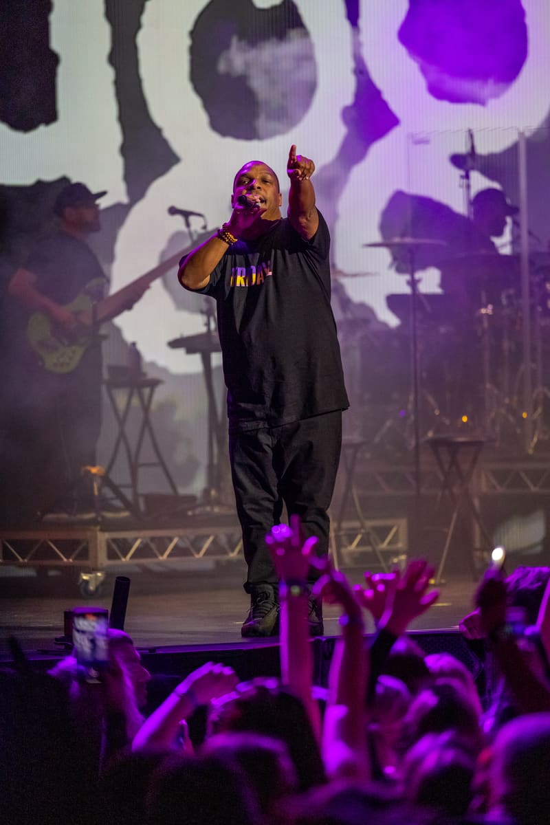 Performer on stage at Illtown Sluggaz – Fridayz Live, illuminated by purple stage lighting, with raised fist and silhouetted band members behind.