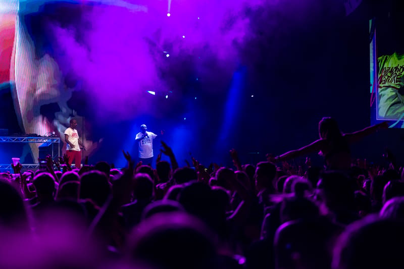 Crowd of fans silhouetted against purple stage lighting during a live music performance.