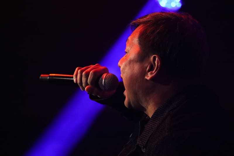 Male performer singing into microphone against deep blue stage lighting.