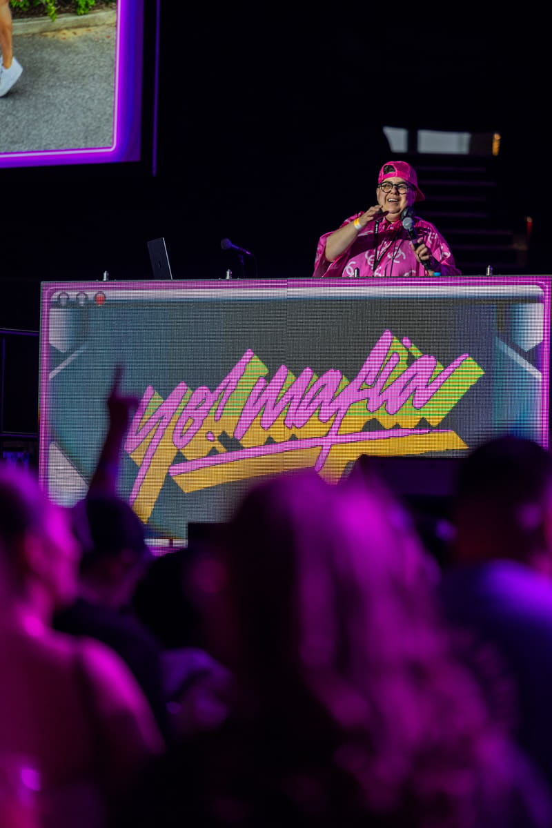 DJ behind illuminated decks with "Yo Mafia" neon signage, audience silhouettes in purple-lit foreground.