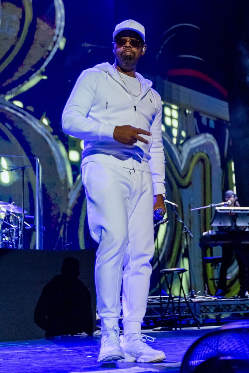 Performer in white outfit and cap on stage under blue lighting during Fridayz Live concert.
