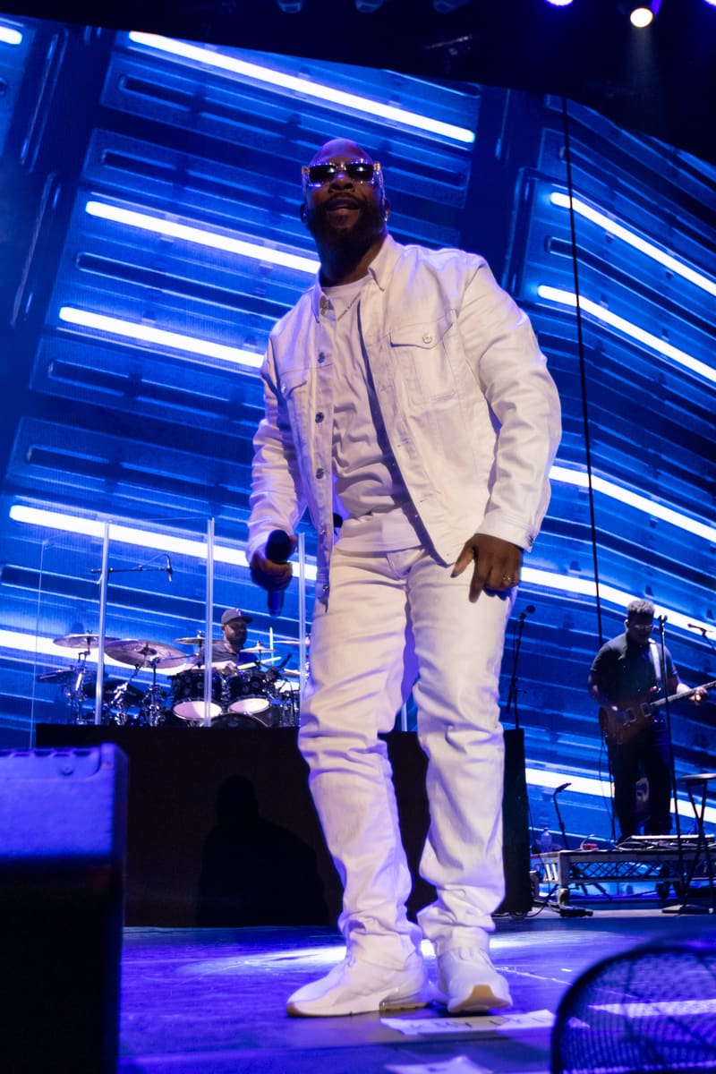 Performer in white suit stands centre stage beneath blue neon lighting during Boyz II Men's Fridayz Live performance.