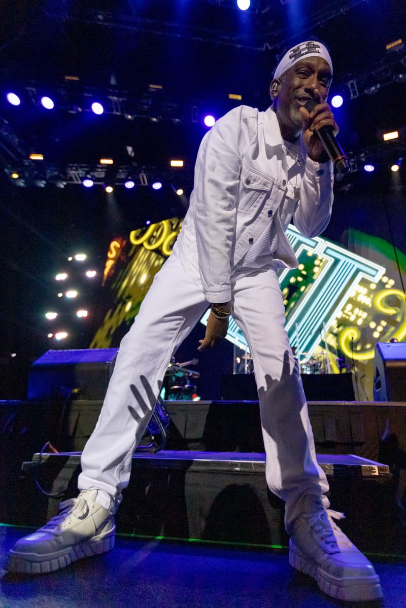 Performer in white outfit singing into microphone on stage under blue spotlights at Fridayz Live.