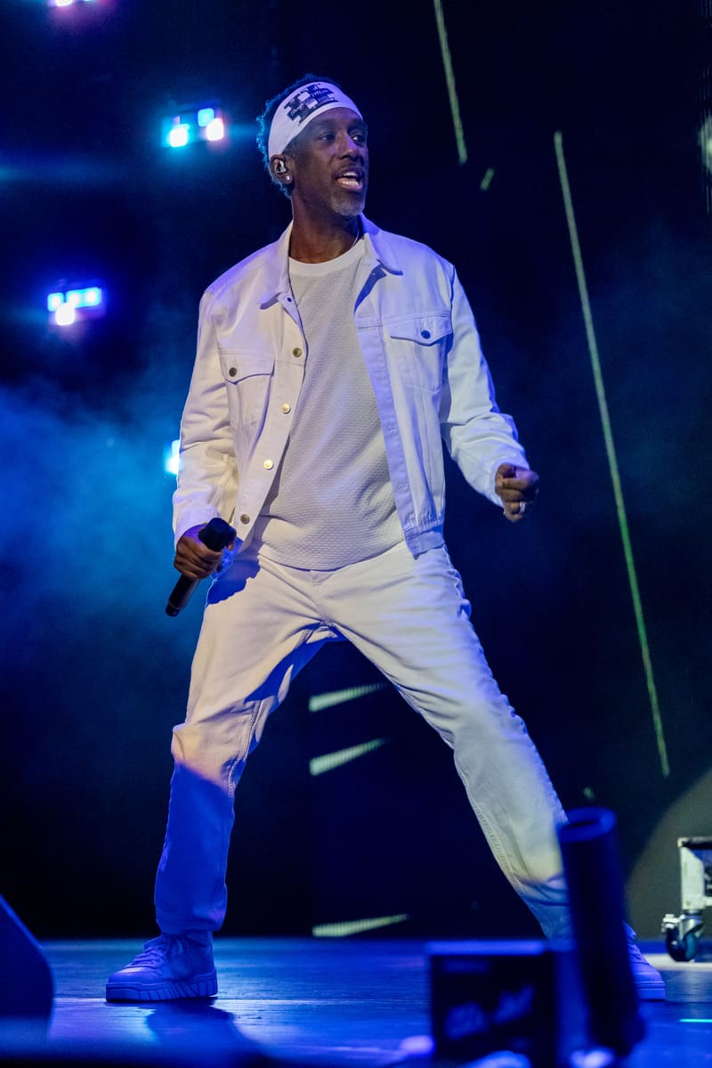 Performer in white jacket and cap holding microphone on stage, bathed in blue stage lighting during Fridayz Live concert.