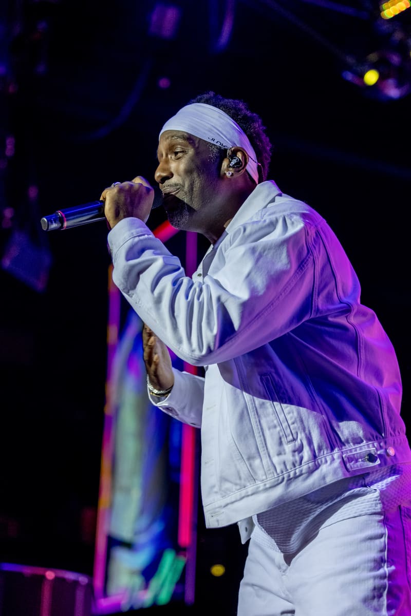 Singer performing at microphone wearing white headband and jacket, bathed in purple stage lighting.