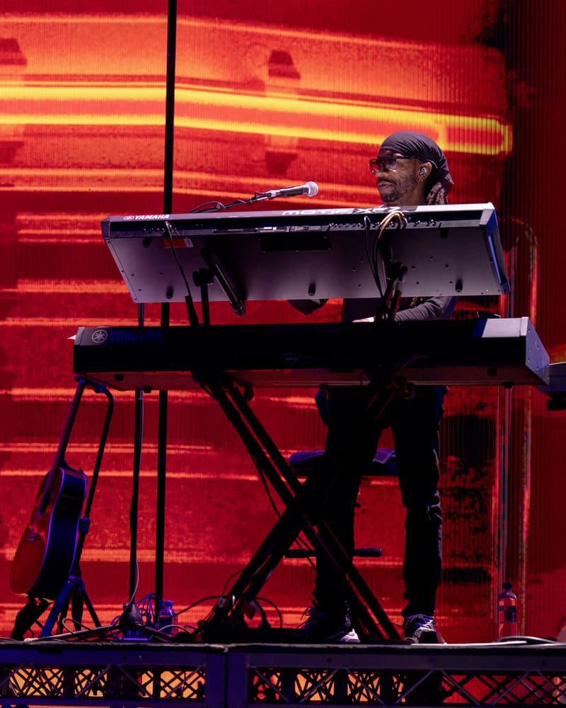 Musician performing at keyboard on stage with vibrant red neon lighting backdrop.