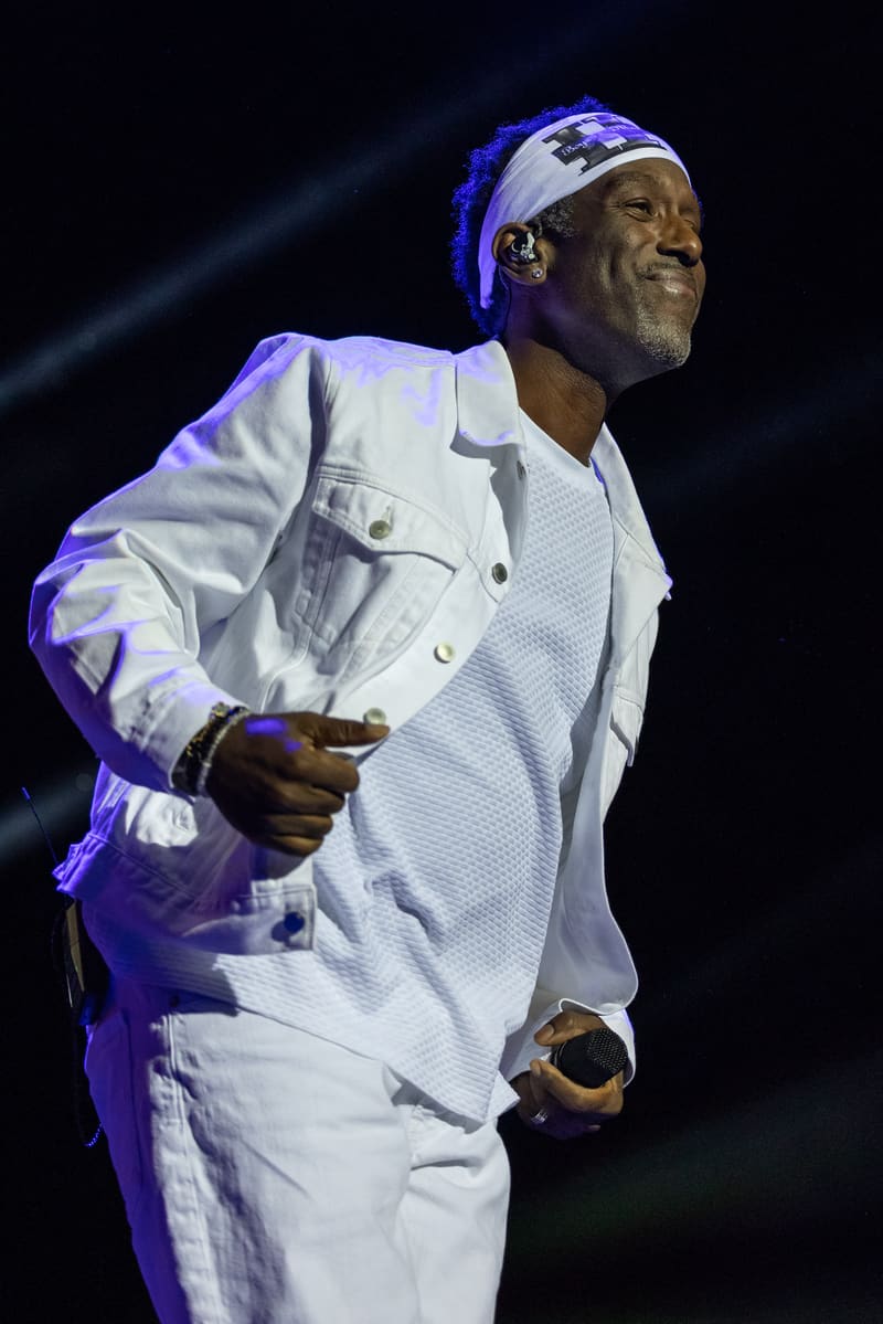 Male performer in white suit and headband singing under blue stage lighting at Boyz II Men – Fridayz Live.