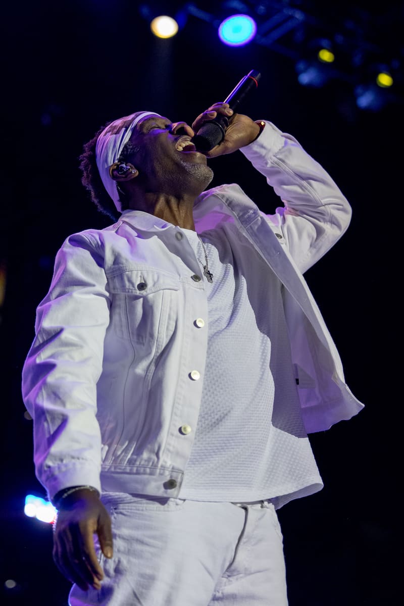 Singer in white jacket performs at microphone under purple stage lighting during Fridayz Live concert.