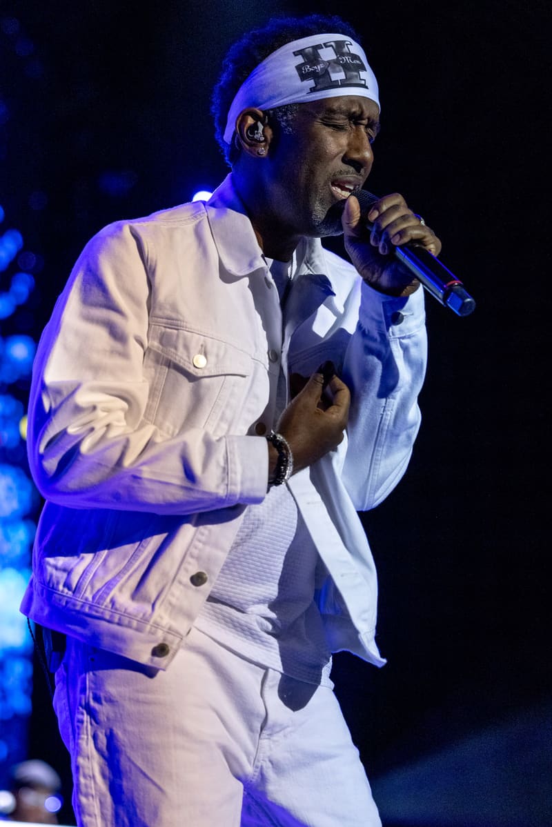 Male performer in white jacket and headband singing into microphone under blue stage lighting.