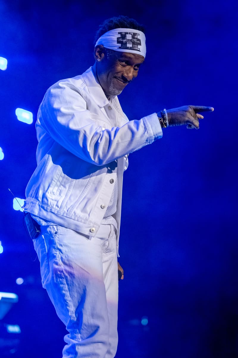 Performer in white suit and headband pointing to audience under blue stage lighting at Fridayz Live.