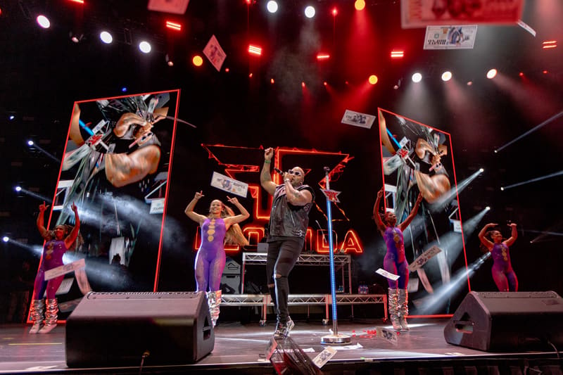 Performer on stage centre with large video screens and colourful stage lighting during Fridayz Live concert.